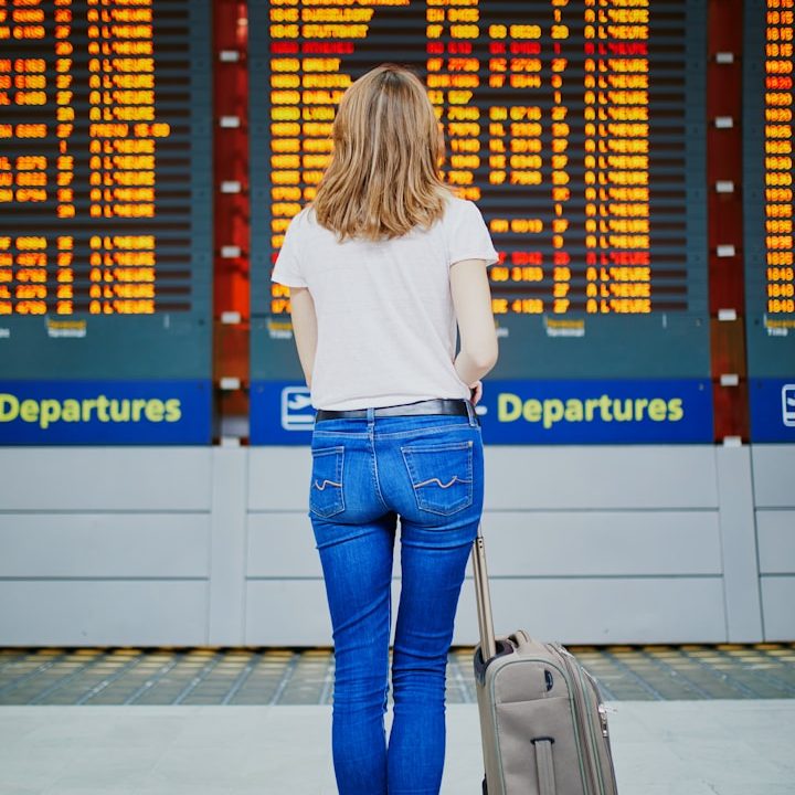 Woman with a suitcase looking at a departure board at an airport.