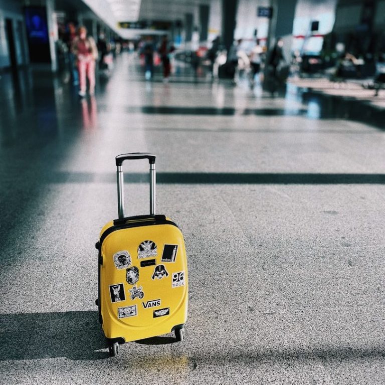 Yellow suitcase covered in stickers, positioned in a busy airport terminal.