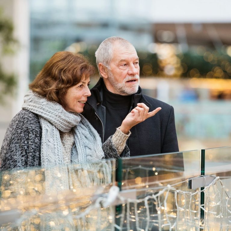 Smiling couple enjoying a conversation near festive lights in a shopping area.